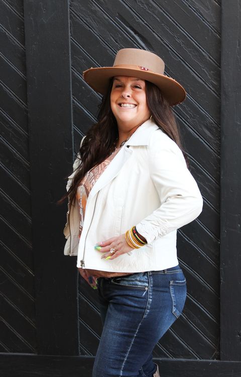 Alison Tolliver, laughing, in a tan wide-brim hat and white jacket, in front of a black wood door