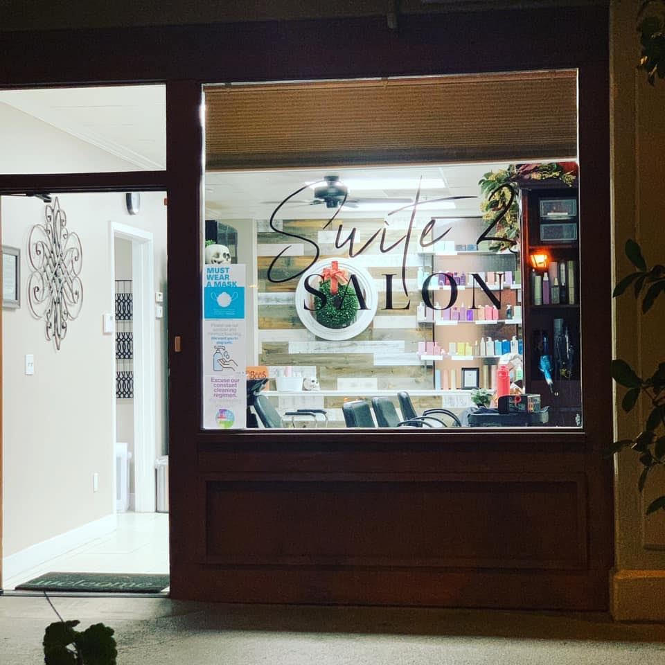 The Suite 2 Salon storefront at night, its script logo on the window and shelves of hair care products glowing inside
